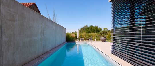 Moderner Gartenpool an Betonwand neben Haus mit Lamellen, Blick ins Grüne